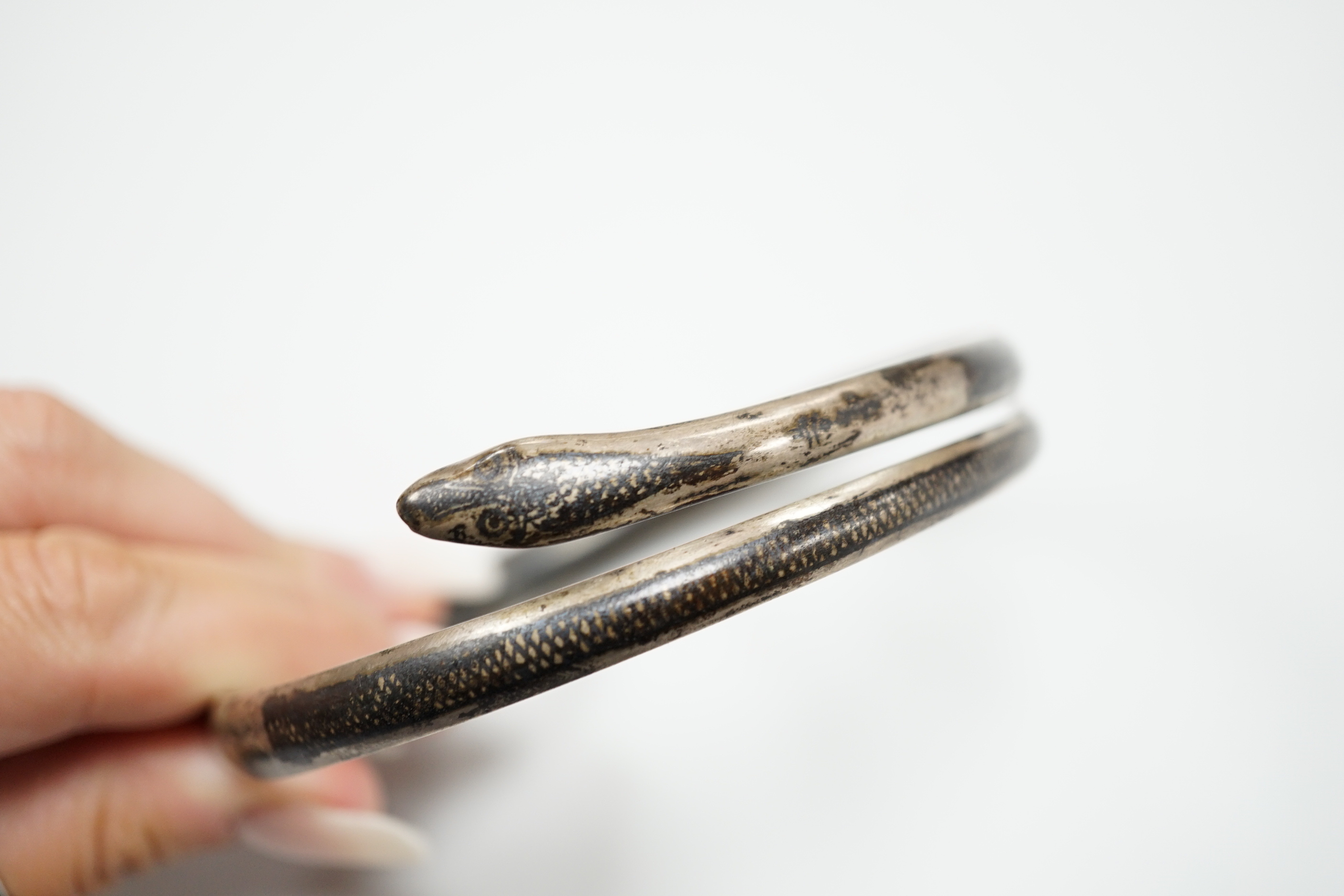 A white metal and niello serpent bangle, decorated with scene of a camel train.